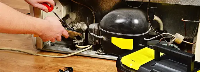 Refrigerator repair technician fixing the compressor and wiring in St Paul, MN